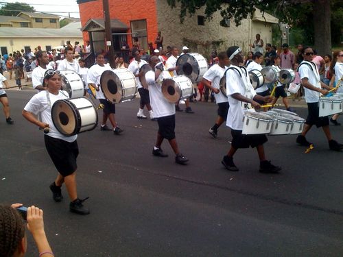 people in a marching band playing the drums through the street as people watch